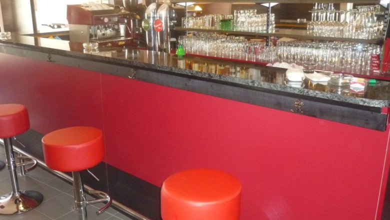 Interior view of a bar with red stools and a well-stocked counter.