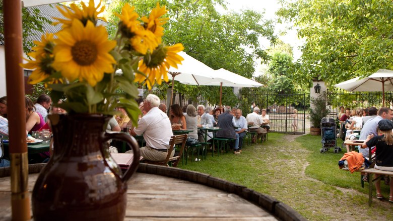 A beer garden with people at tables, parasols and sunflowers in a jug in the foreground.