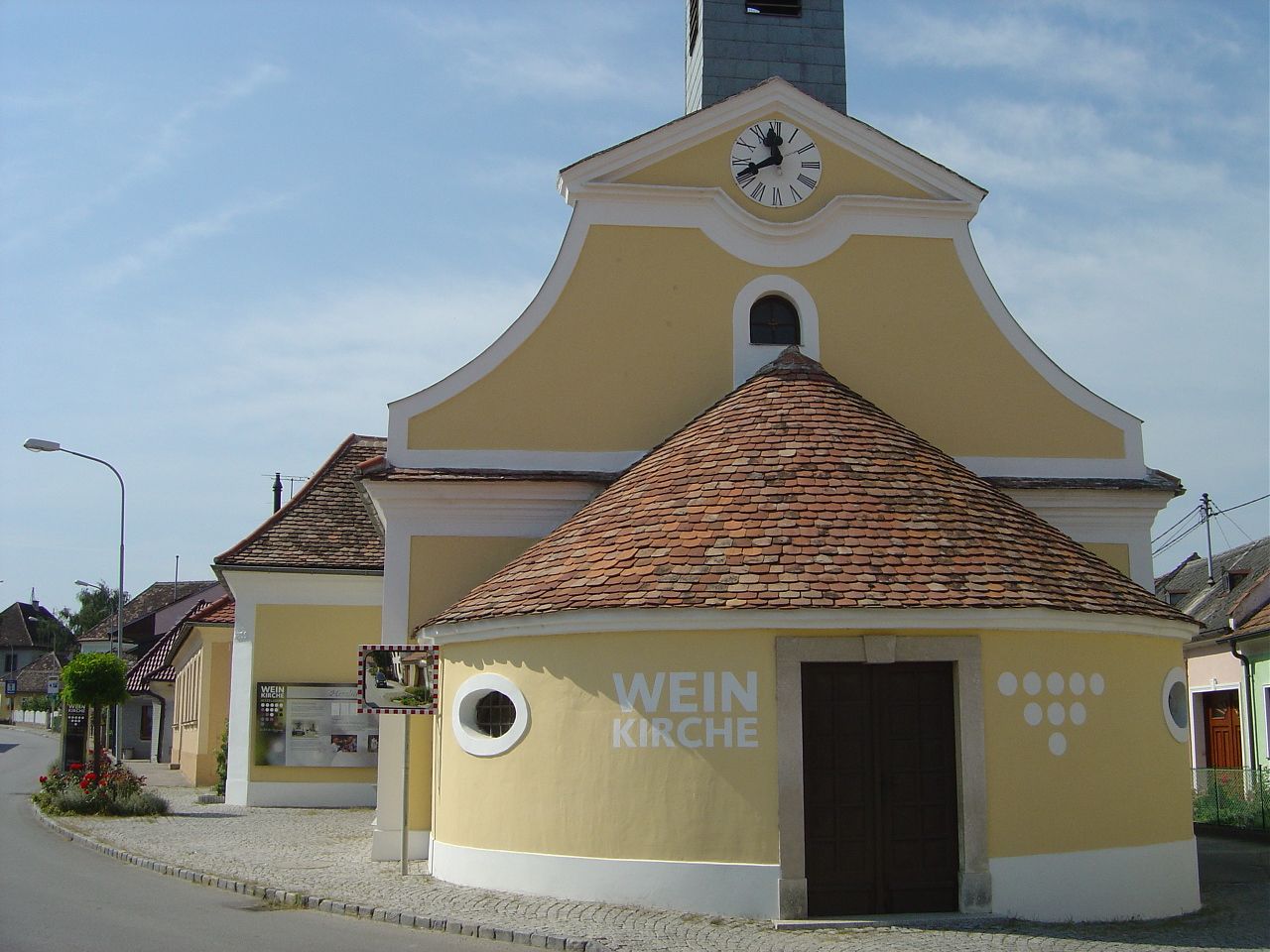 Yellow church with clock tower and the inscription 'Weinkirche' in a village.