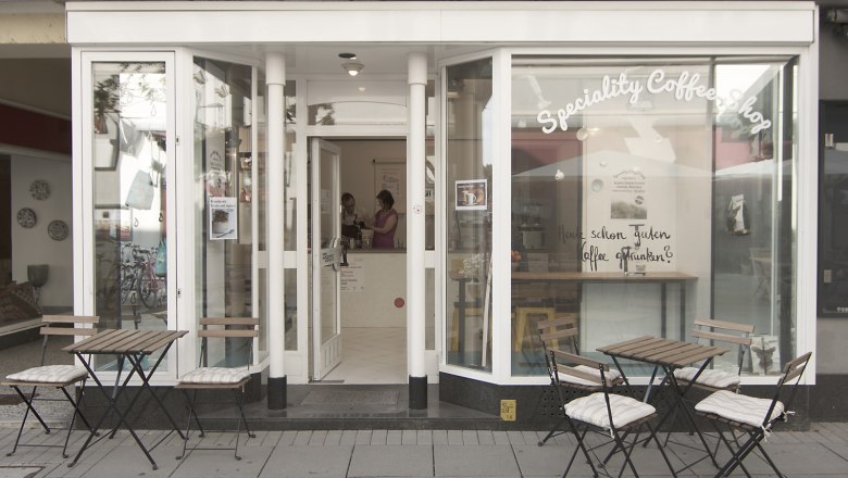 Exterior view of a café with tables and chairs on the sidewalk.
