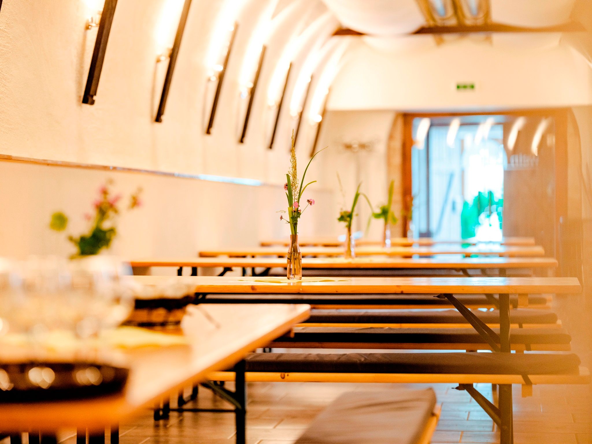 Interior view of a Buschenschank (typical tavern) with long wooden tables and benches, decorated with flower vases.