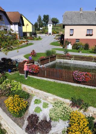 A well-kept garden with flower beds and a small pond in a village.
