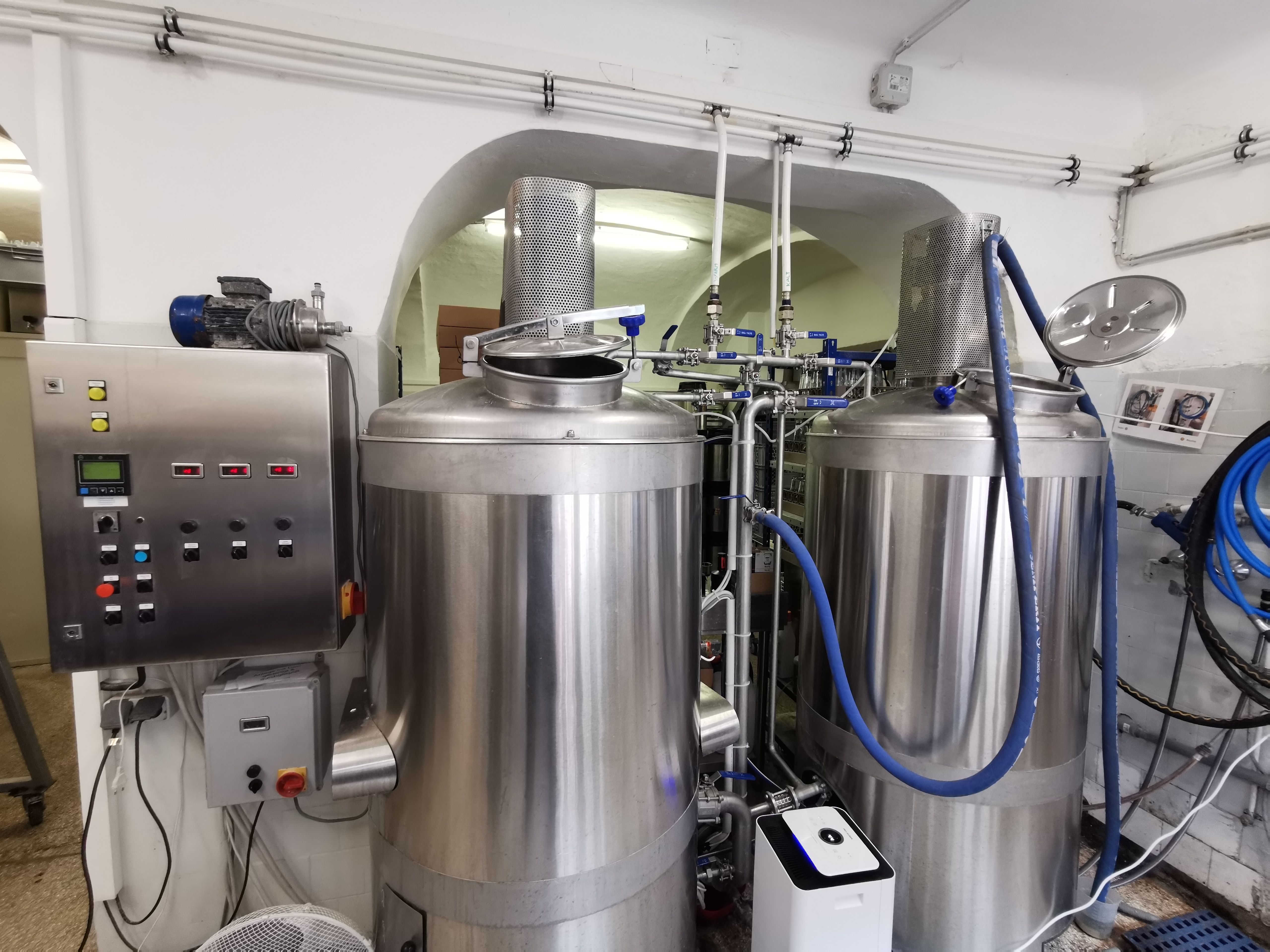Two large stainless steel brewing kettles in a brewery with control panel.