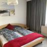 Bedroom with double bed, gray bed linen, red throw and pillows, lamp and beach picture on the wall.