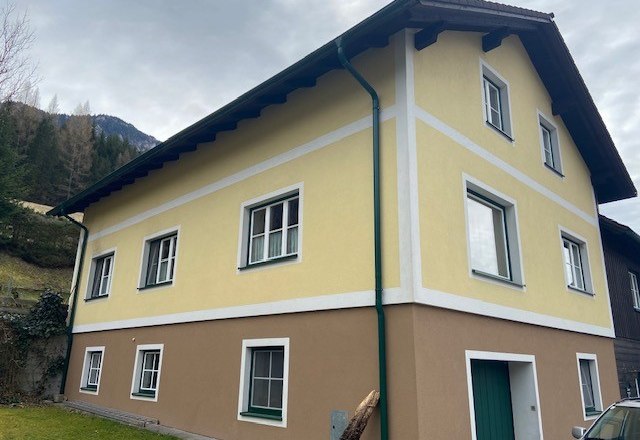 Two-storey yellow-brown house with white window frames and green downpipes.