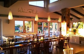 A cozy guest room with wooden tables and chairs, decorated with candles and plants, illuminated by warm sunlight.