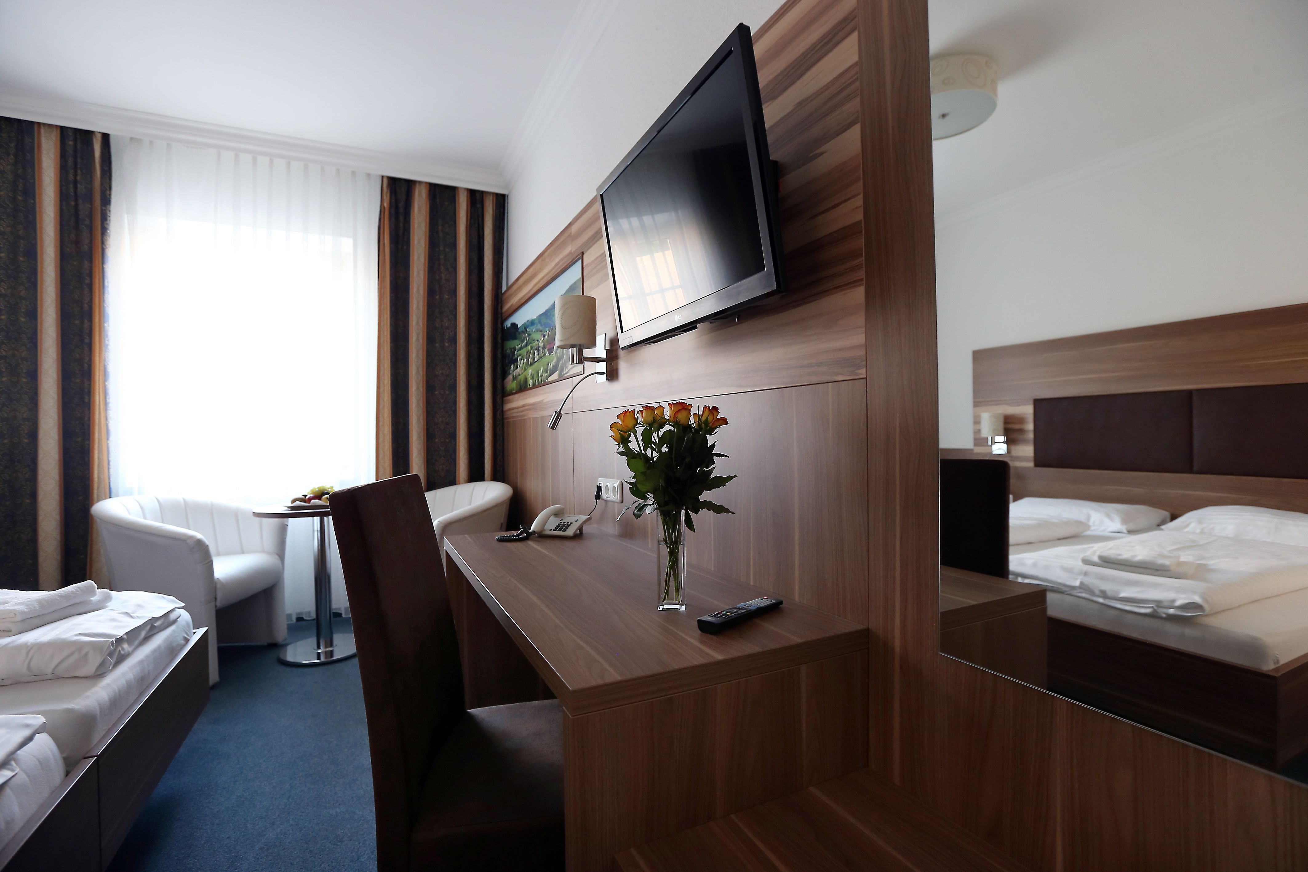 Modern furnished hotel room with double bed, desk, flat screen TV and bouquet of flowers.