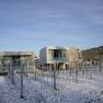 Modern garden lofts covered in snow in winter, surrounded by bare trees and a clear blue sky.