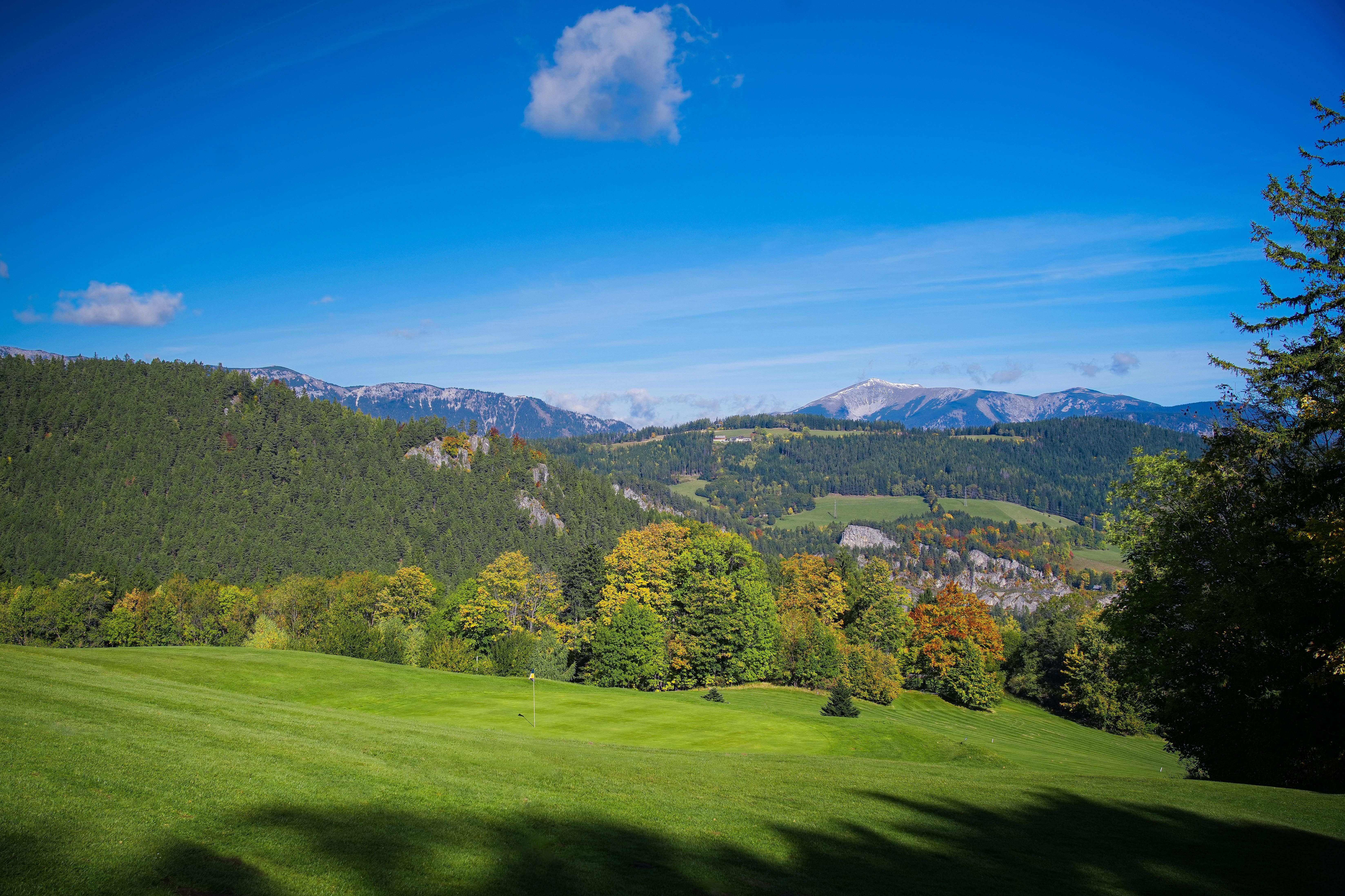 View of a green landscape with hills and mountains in the background, under a clear blue sky.