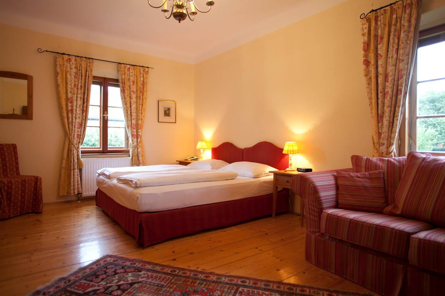 Cozy bedroom with double bed, red headboard, striped sofa and curtains, wooden floor and carpet.
