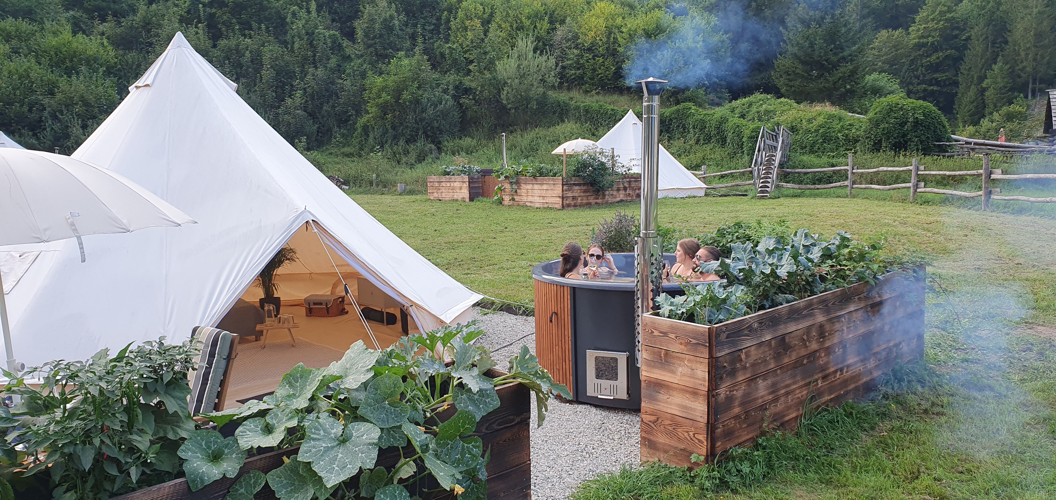 Glamping tents and hot tub in green surroundings.