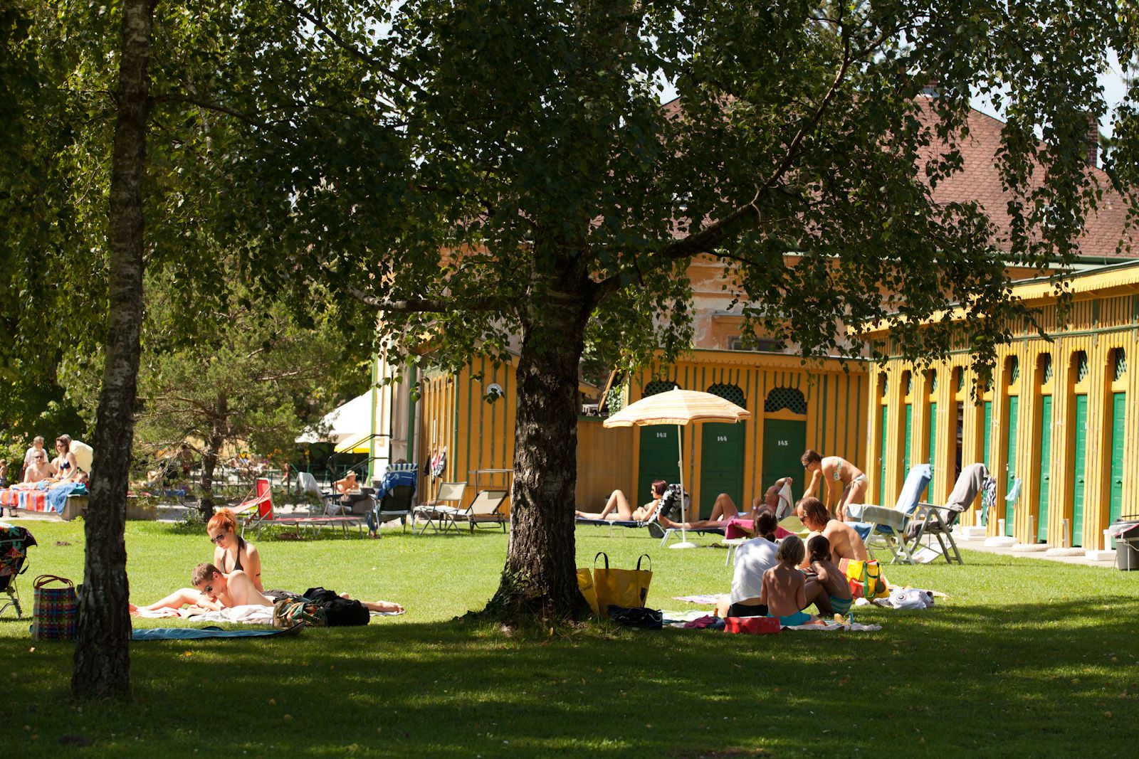 People relaxing on a lawn in front of a historic bathhouse.