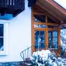 Winter view of the house with wooden veranda and snow-covered plants.
