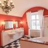 Elegant bathroom with red walls, two washbasins, bathtub, shower and chandelier.