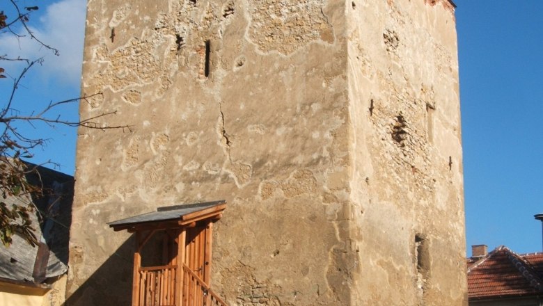 An old defense tower with wooden stairs and railings, surrounded by buildings, under a blue sky.
