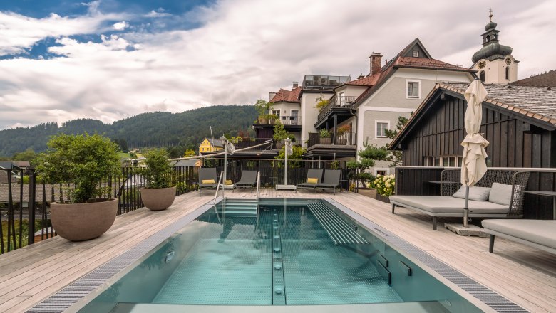 A modern pool on a terrace with a view of the surrounding houses and wooded hills in the background.