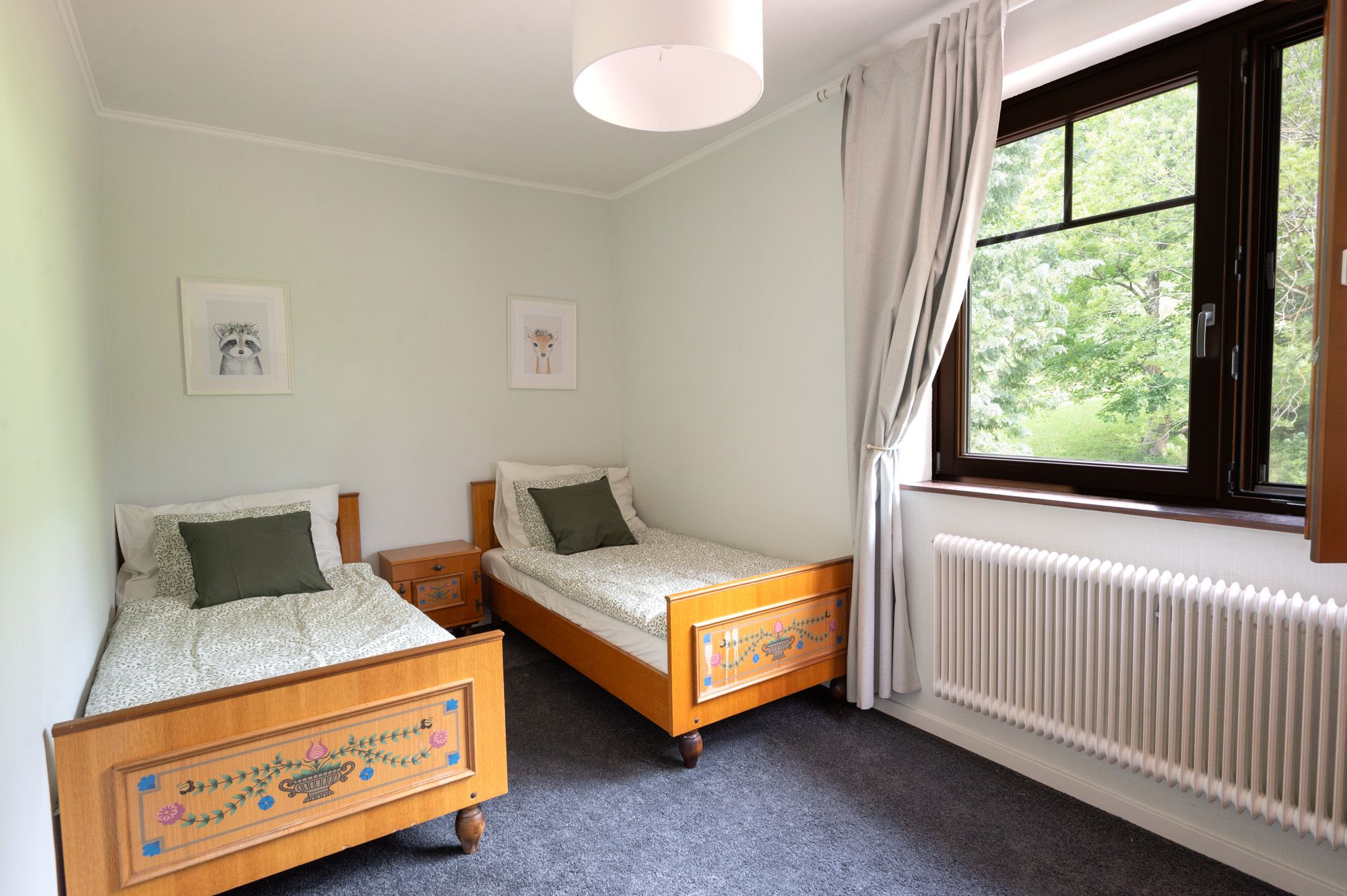 Bedroom with two single beds, wooden furniture and a large window with a view of the greenery.