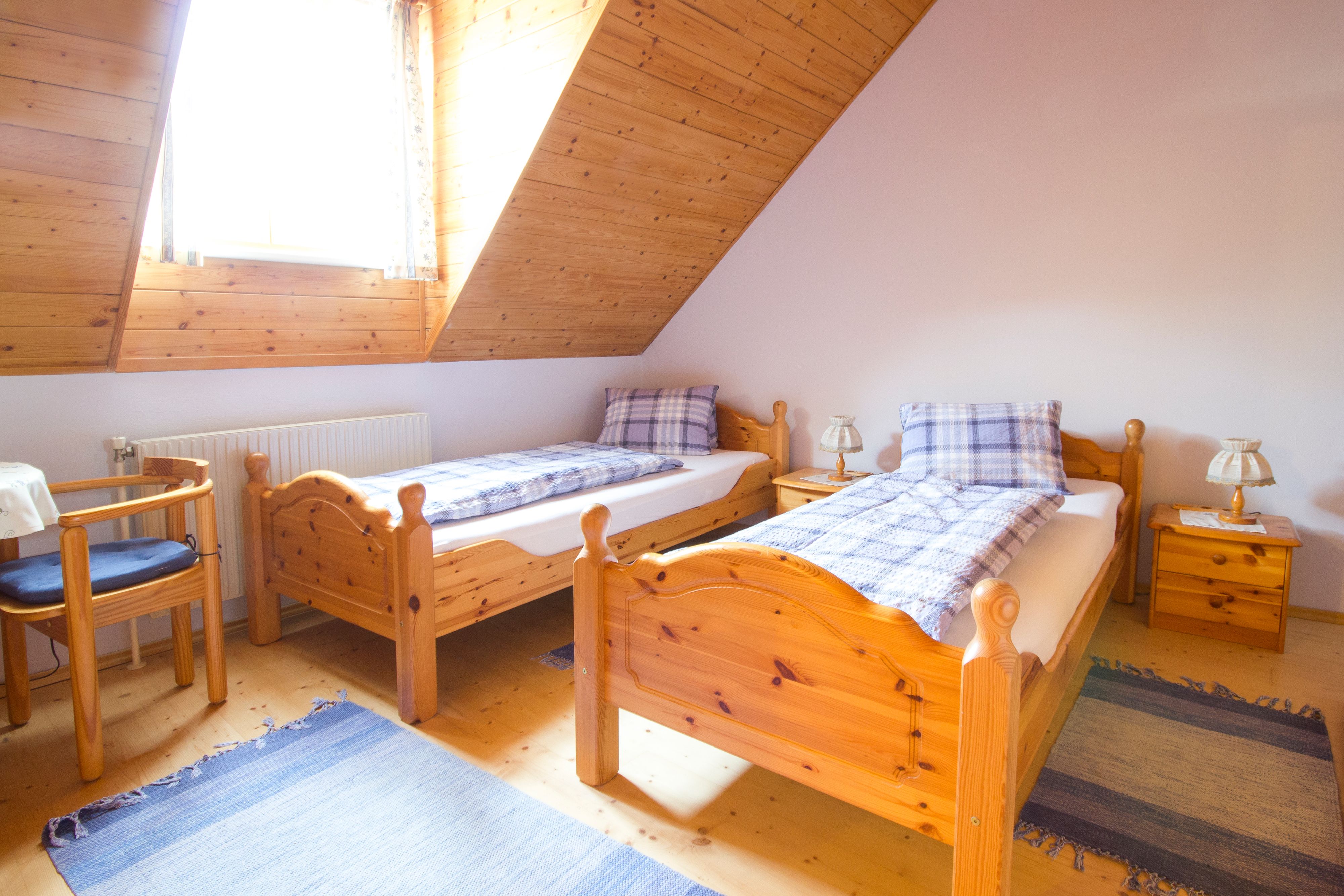 Cozy bedroom with two single beds made of wood, blue carpets and a window with wooden paneling.