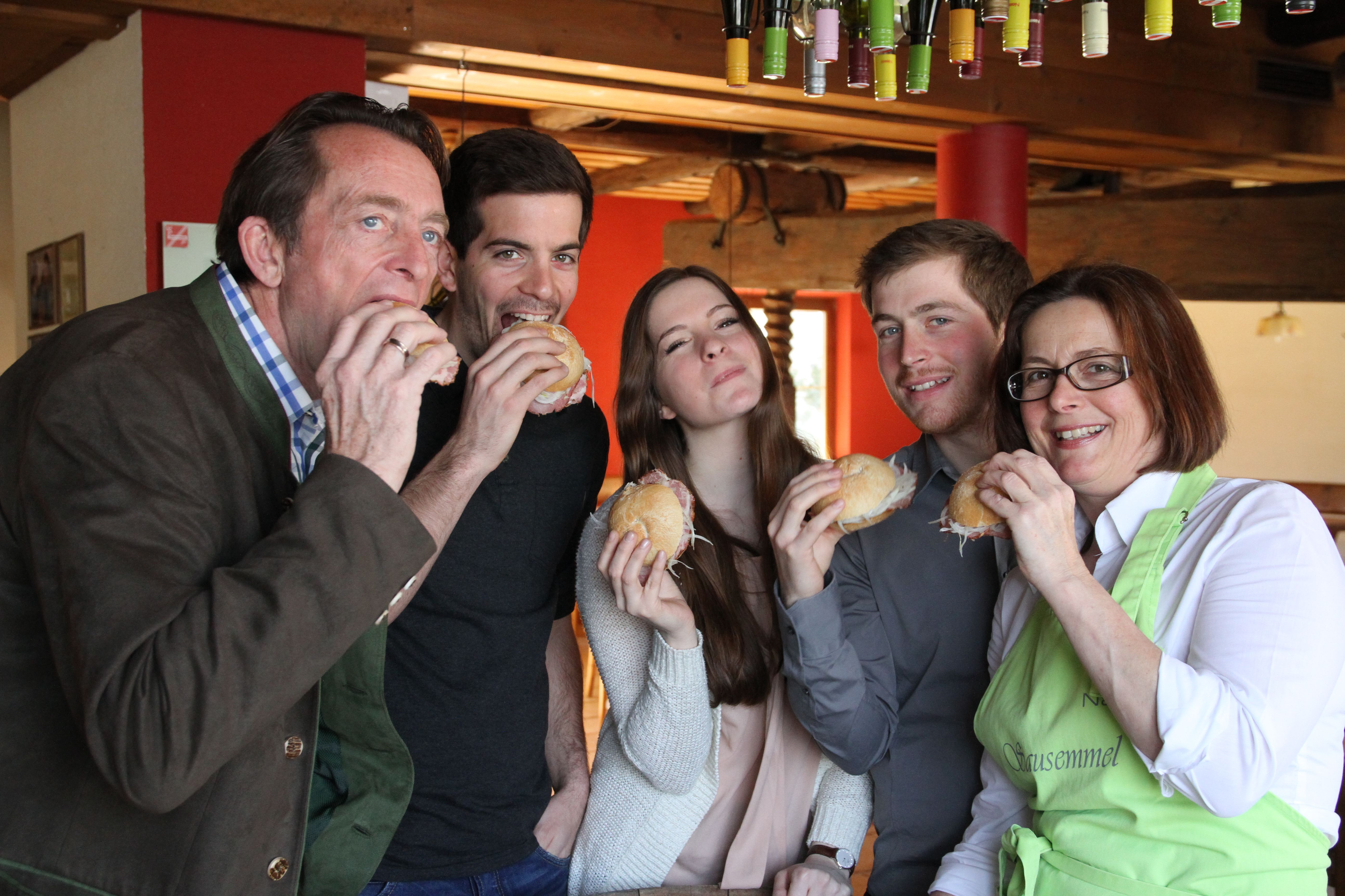 Five people eat sandwiches together in a cozy room.