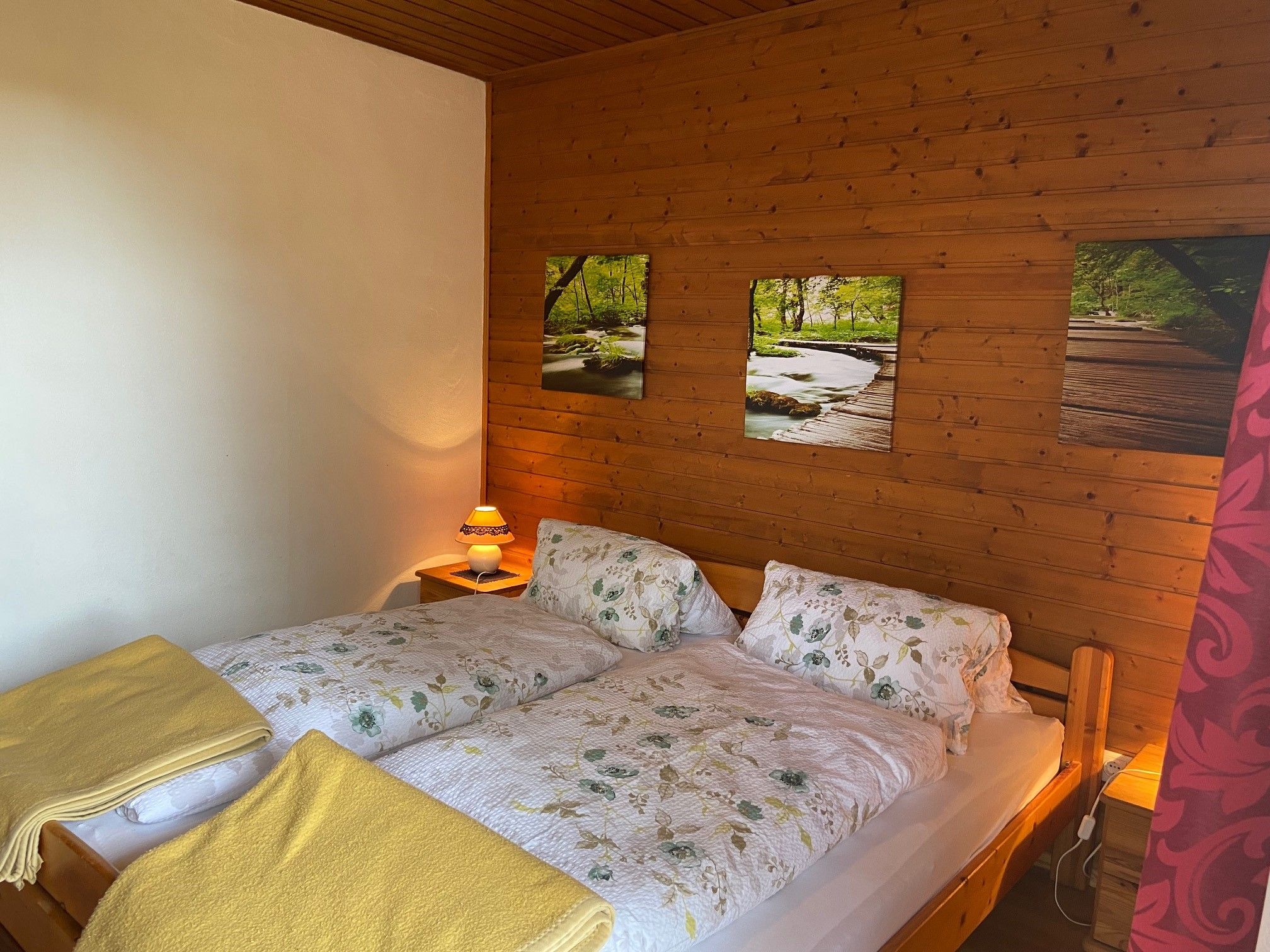 Cozy double room with wooden walls, a double bed with floral bedding and yellow blankets, as well as a bedside lamp.