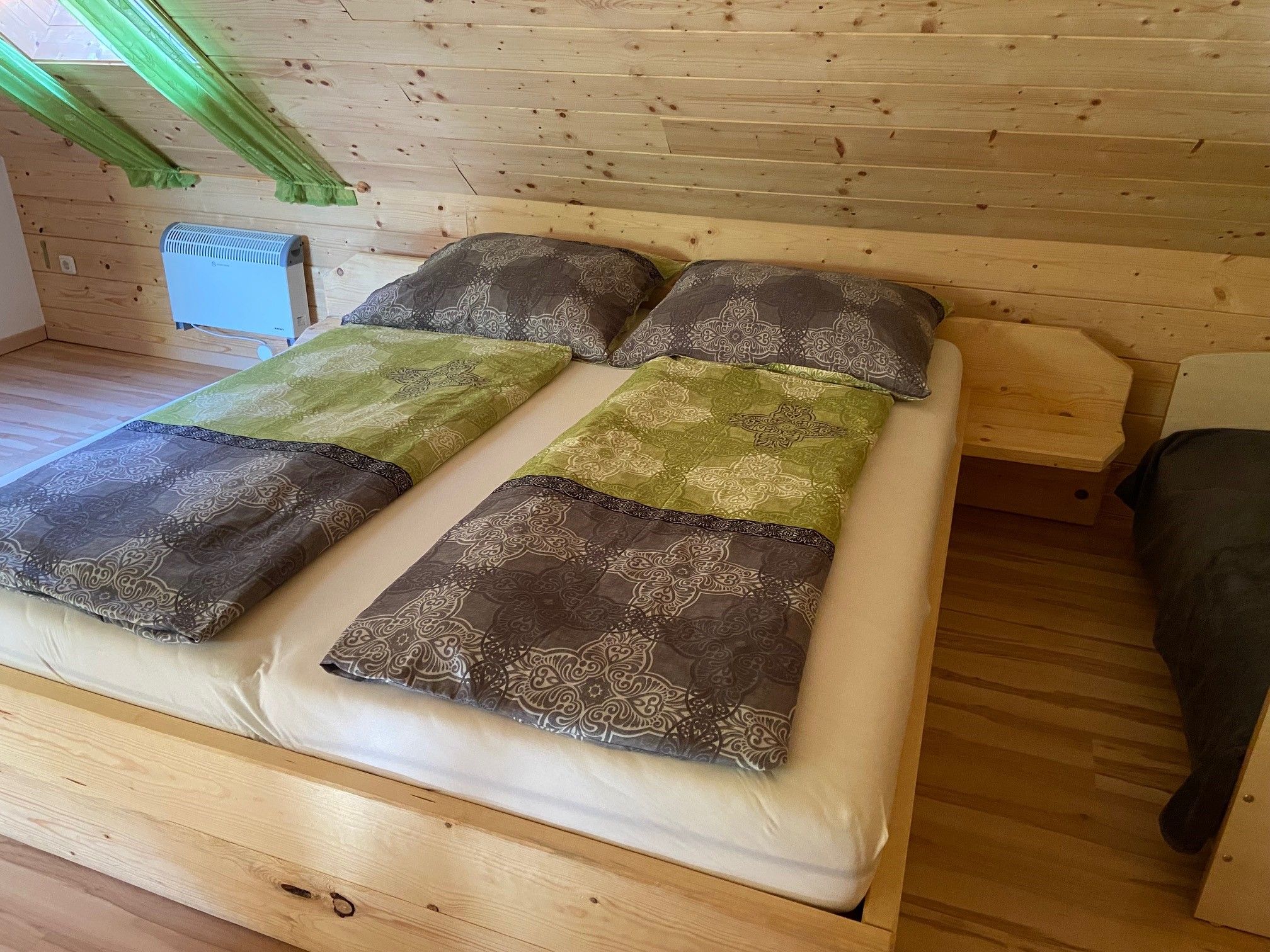 Double bed in a room with wooden paneling and green curtains.