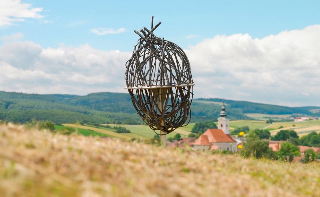 Metal art installation in a rural landscape with a church in the background.
