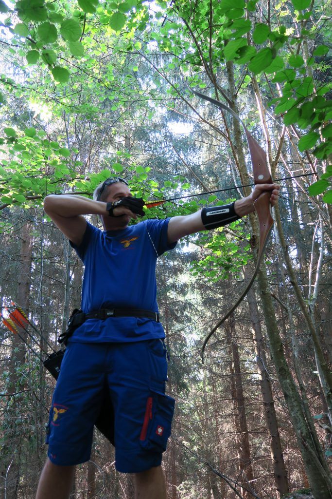 An archer takes aim with a bow in the forest.