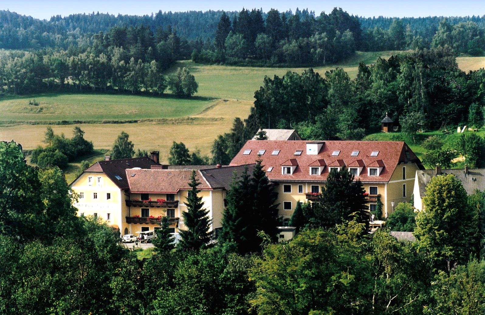 A large building with red roofs in a green, wooded landscape.