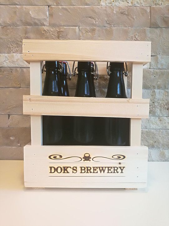 Wooden crate with three dark beer bottles from Dok's Brewery in front of a stone wall.