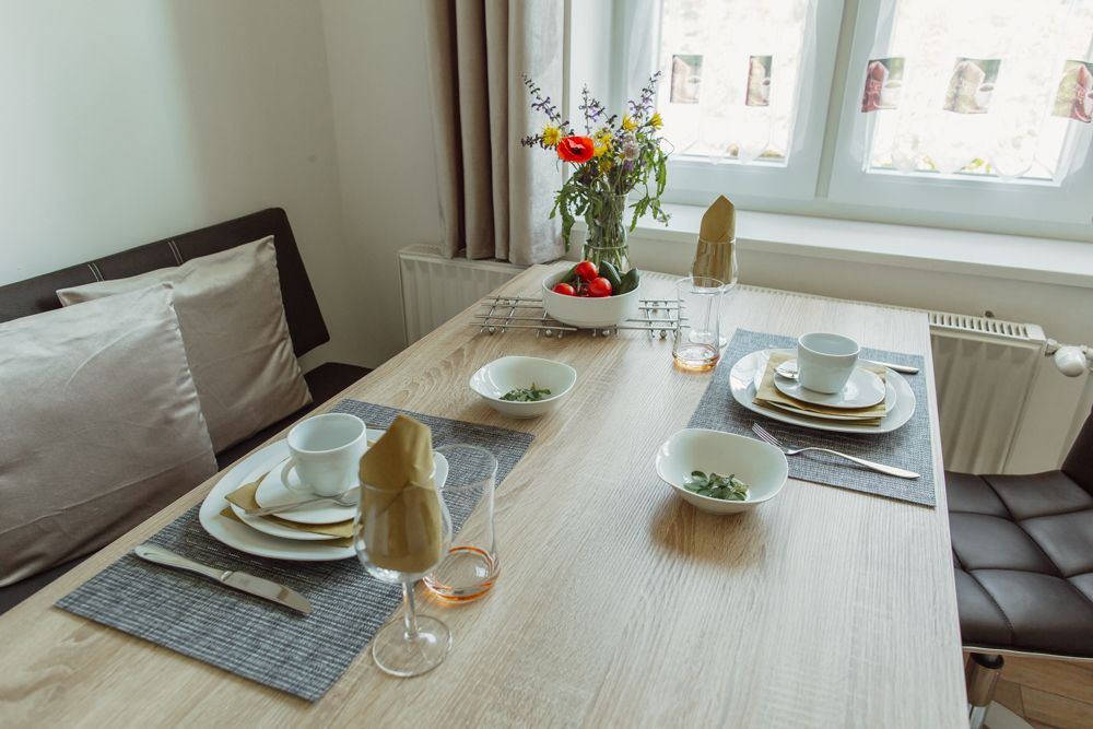 A dining table set with crockery, glasses and flowers in a bright room.