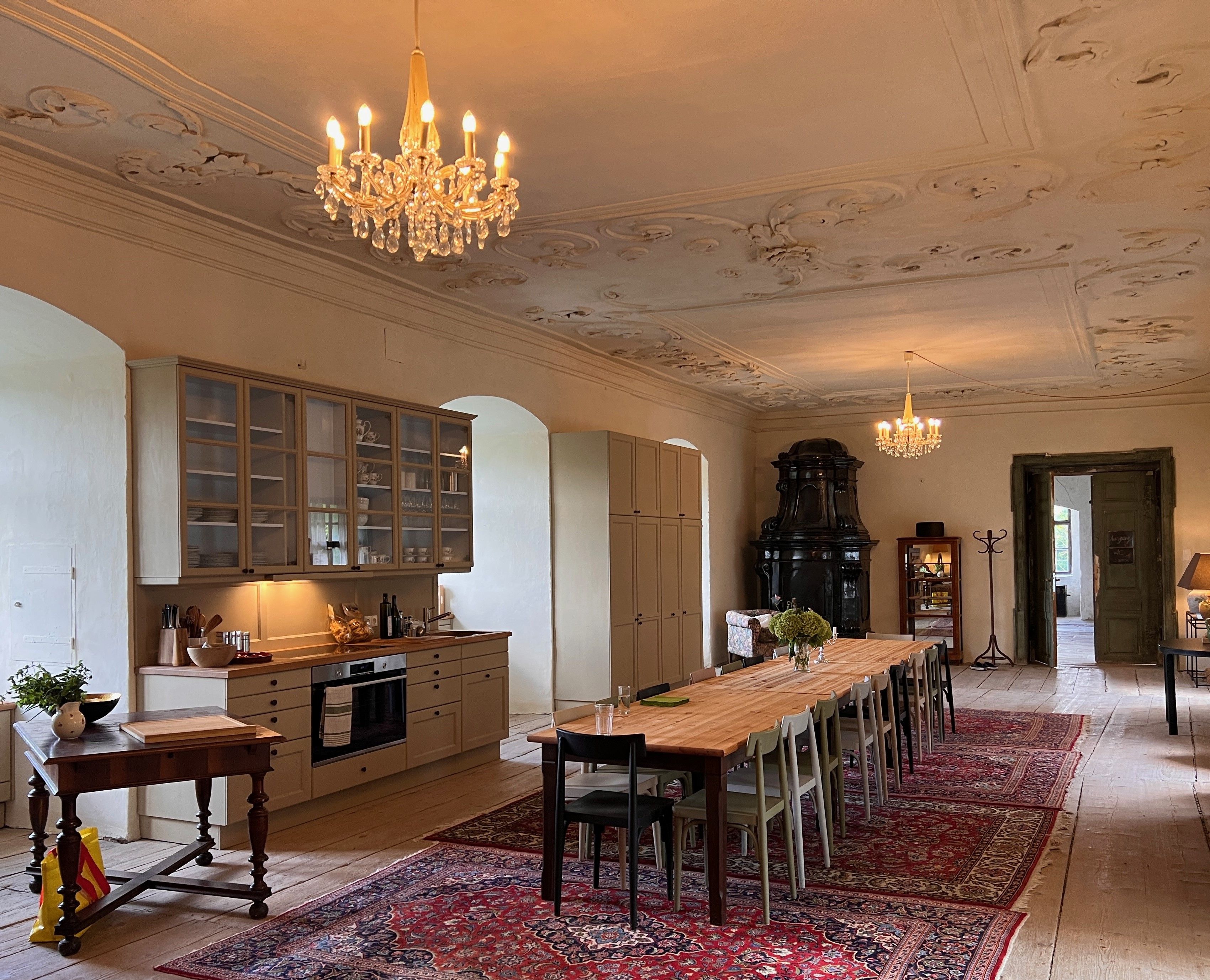 Elegant dining room with long wooden table, chandeliers and antique stove.