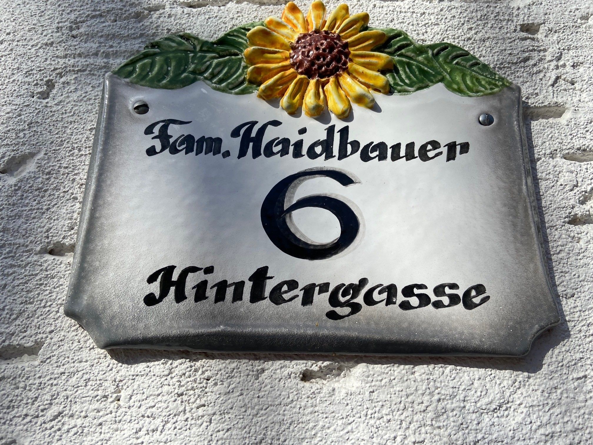 House number sign with sunflower and the inscription 'Fam. Haidbauer 6 Hintergasse'.
