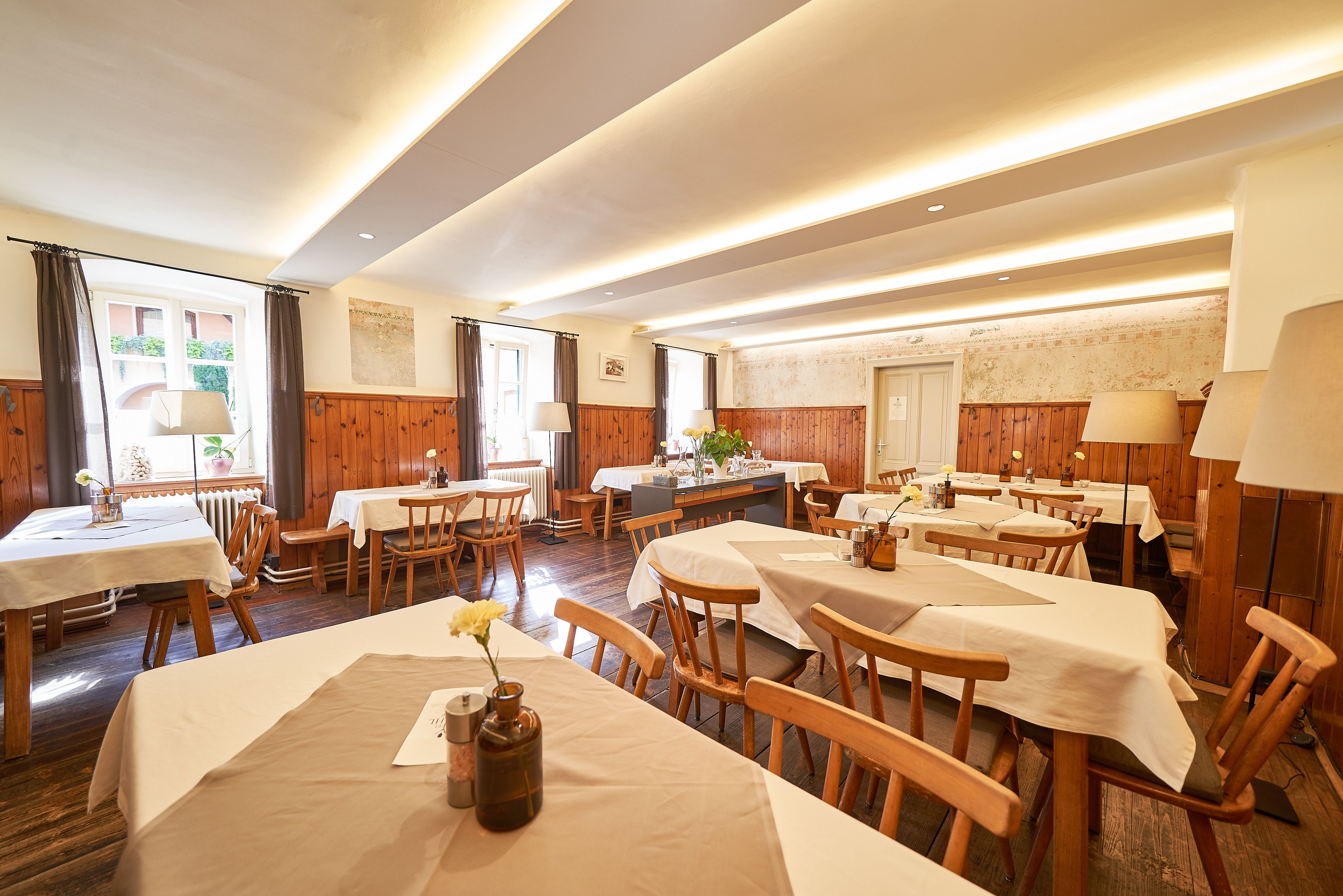Interior view of a cozy dining room with wooden furniture and white tablecloths.
