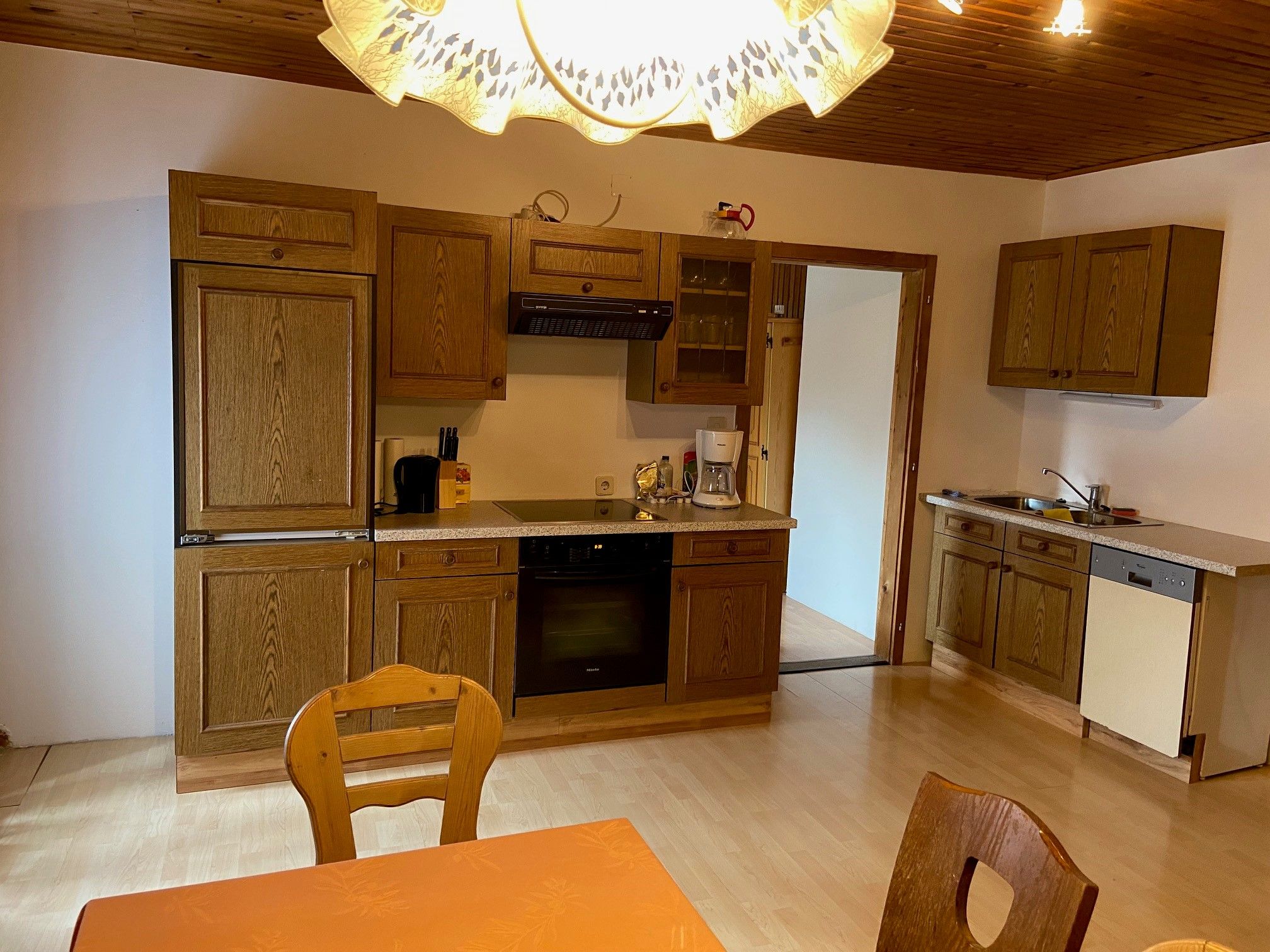 Kitchen with wooden furniture, dining table and chairs, stove, sink and dishwasher.