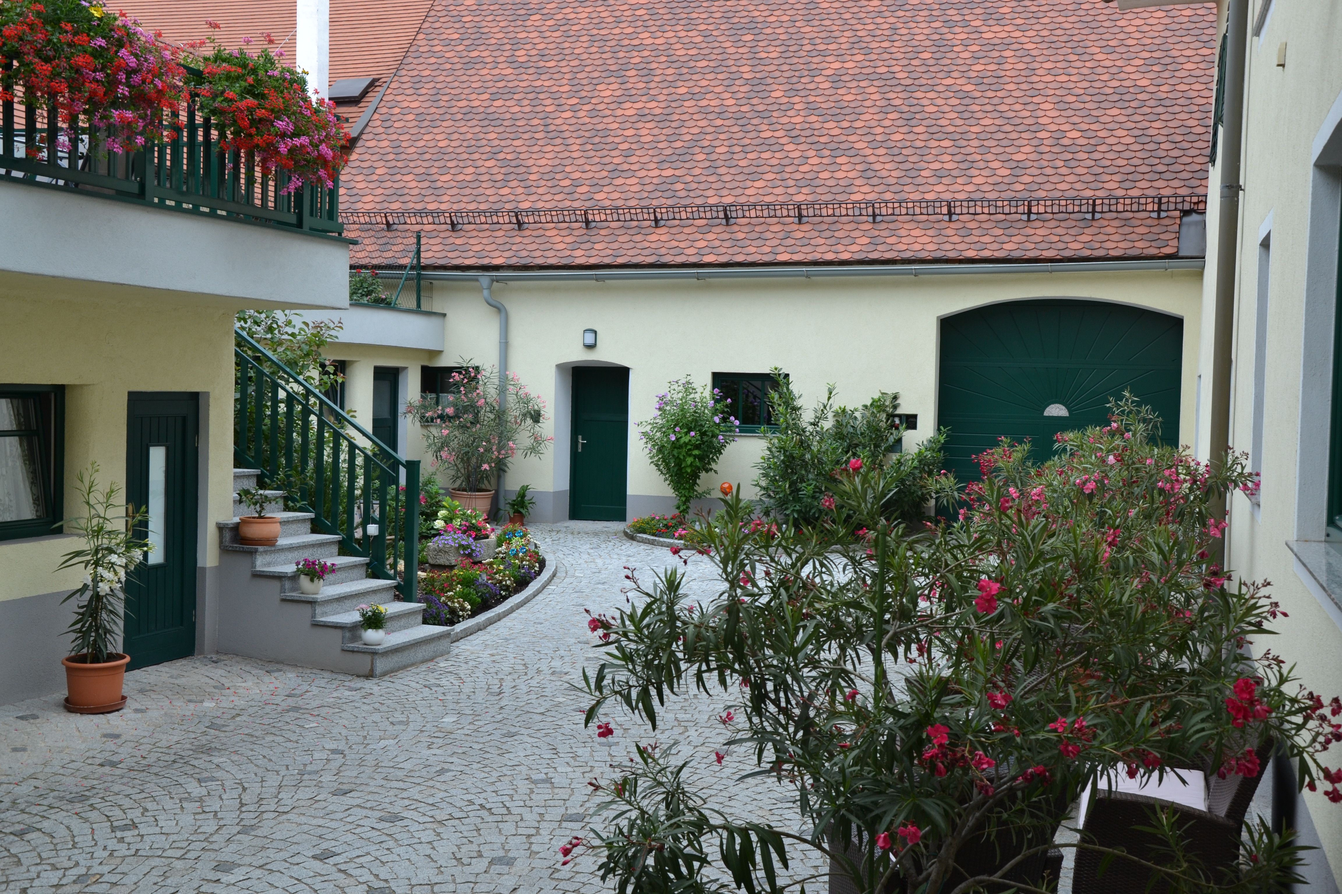 A well-tended courtyard with flowers and plants, surrounded by buildings with red tiled roofs and green doors.