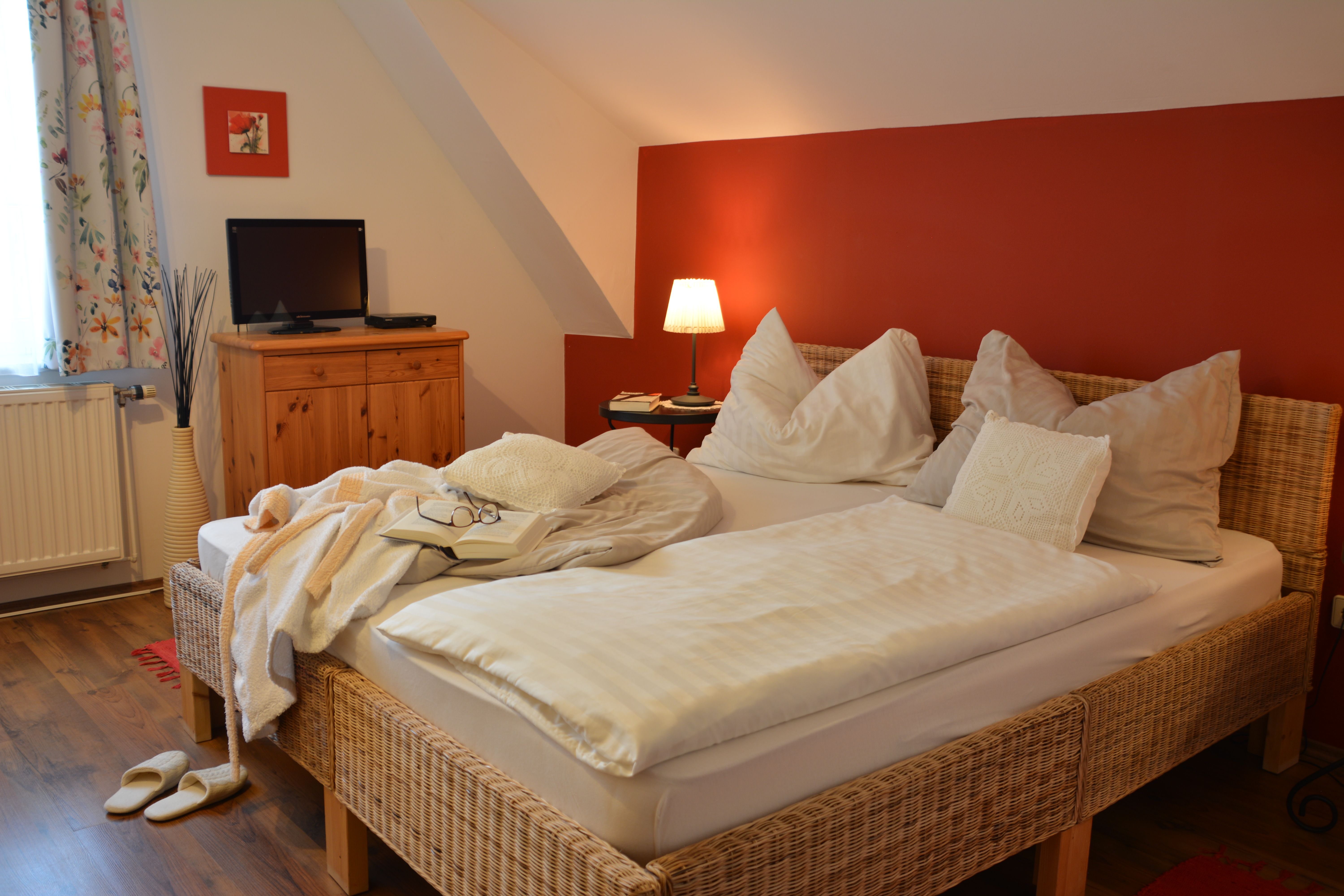 Cozy double room with red wall, bed, bedside lamp, TV and wooden furniture.