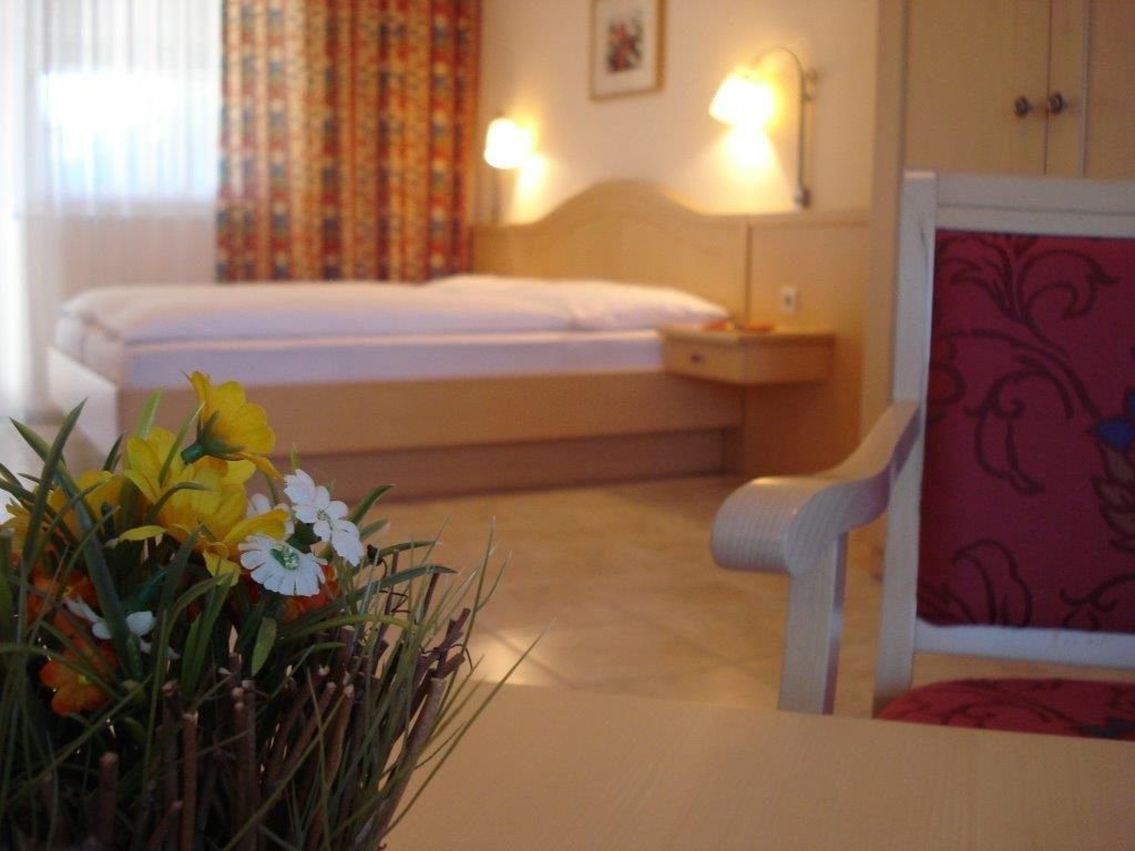 A cozy guest room with a bed, a chair and a table with flowers.