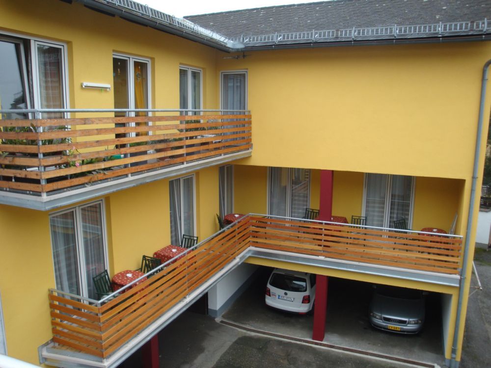 Yellow building with balconies and parked cars underneath.