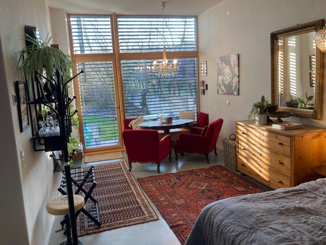 Living room with large windows, red armchairs, wooden furniture and carpets, view of the garden.