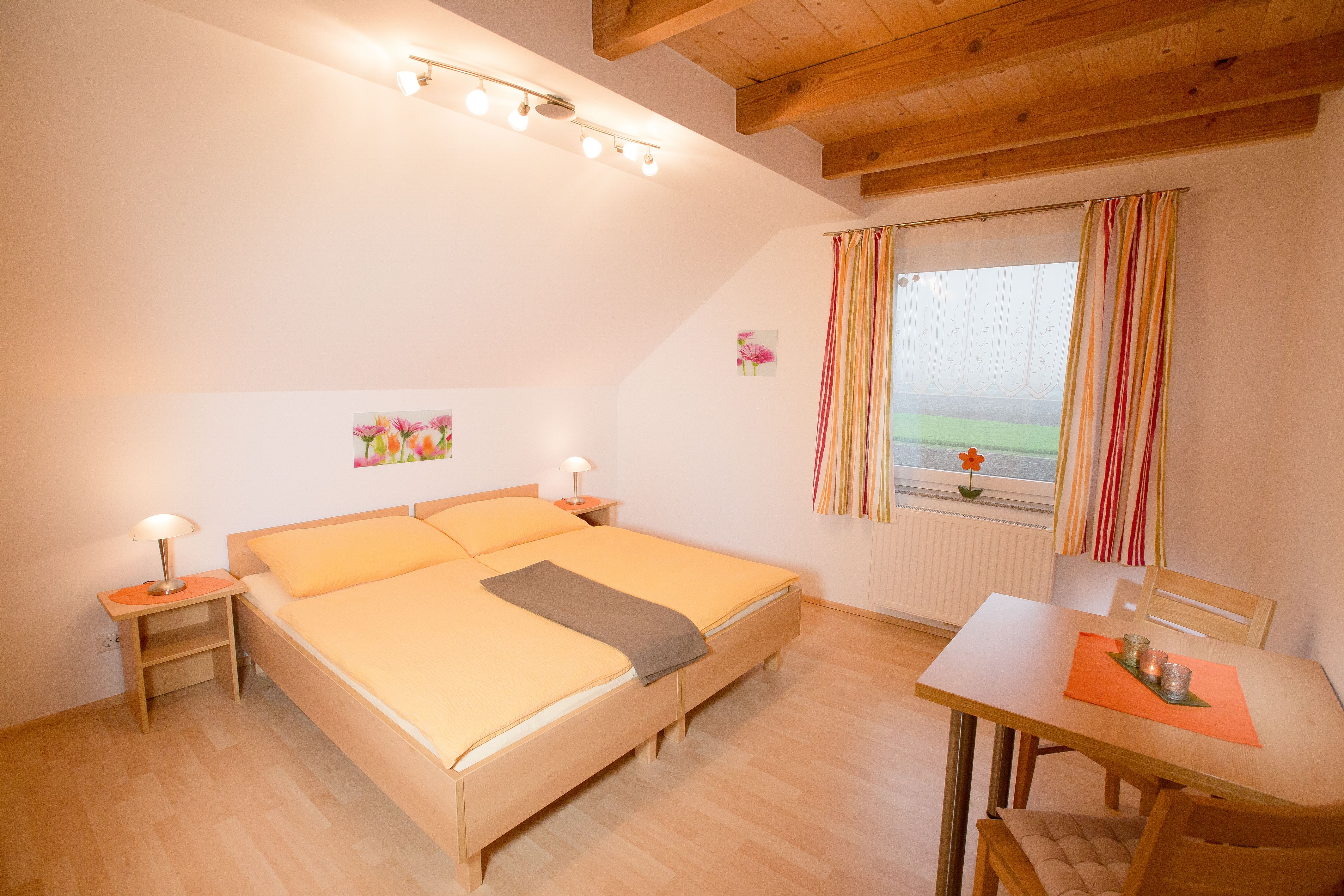 Cozy bedroom with double bed, wooden beamed ceiling and table with chairs.