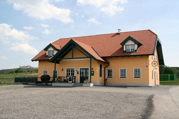 A yellow house with a red roof and green accents, surrounded by a rural landscape.