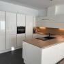Modern kitchen with white high-gloss cabinets, wooden worktop and built-in oven.