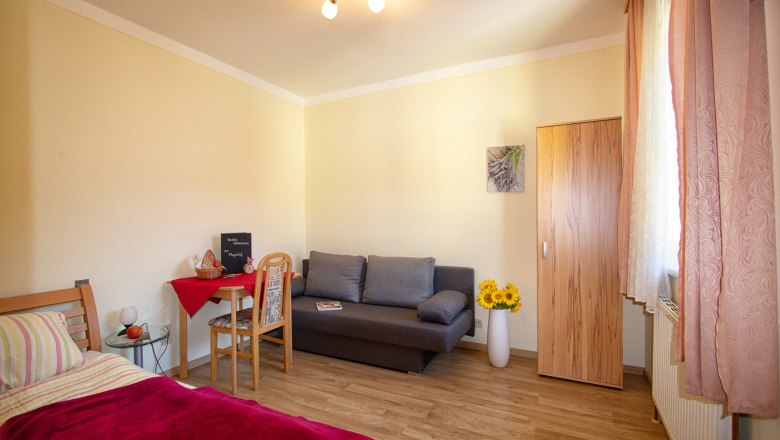 Cozy room with bed, sofa, table and wardrobe, decorated with sunflowers and a picture on the wall.