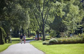 A couple walks along a path in the spa gardens of Bad Sch&ouml;nau, surrounded by green trees and well-tended flowerbeds.
