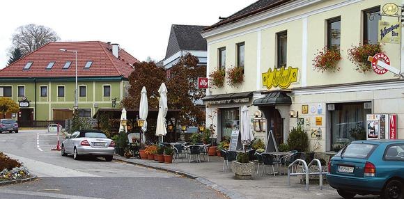 Gasthof Mostlandl exterior view, © Leopold Rank Exterior view of an inn on a lively square with trees, parasols, armchairs and much more.