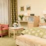 Cozy hotel room with green carpet, red armchair, table with champagne cooler, flowers and bed with green throw.