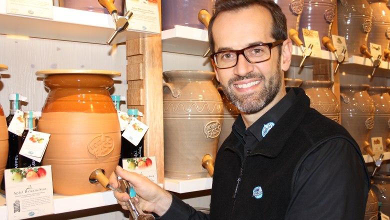 A man fills a bottle from a large ceramic barrel at Vom Fass.