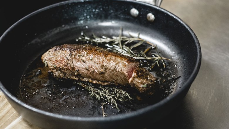 Roasted piece of meat with herbs in a pan.