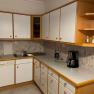 Kitchen with white cupboards, sink, coffee machine and tiled splashback.