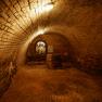 A vaulted brick cellar with a barrel and an illuminated shelf in the background.